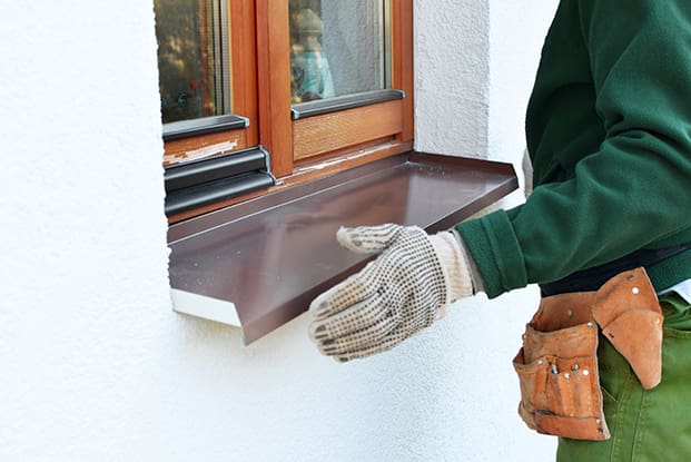 Nahaufnahme eines modernen beigen Backsteinhauses mit großen Dreiecksfenstern und einem steilen Satteldach vor einem strahlend blauen Himmel.