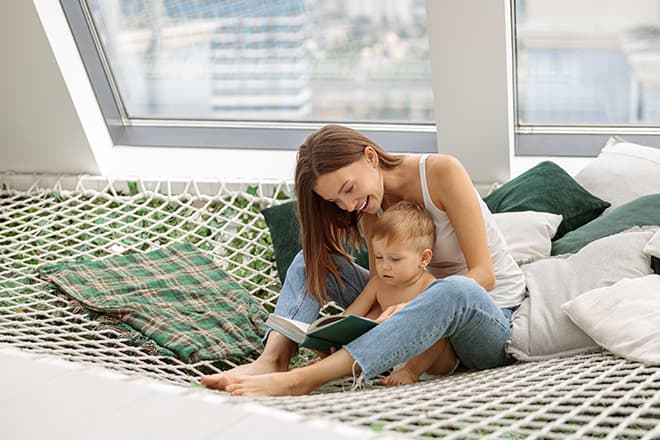 Eine Frau sitzt mit einem Kind auf dem Schoß auf einem Bett und liest ein Buch